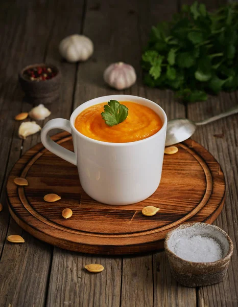 Pupmkin cream soup in cup on brown wooden table, vertical, side