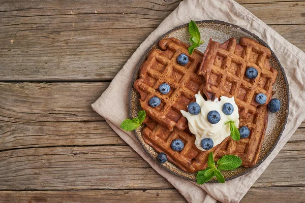 Chocolate banana waffles with blueberries, on dark wooden old ta