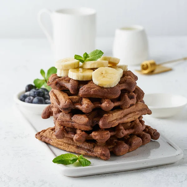 Chocolate banana waffles with maple syrup on white table, close
