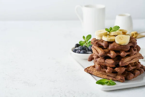 Chocolate banana waffles with maple syrup on white table, copy s