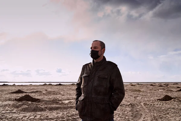 Apocalypse and cataclysm due to coronavirus. Mature man in black mask and black coat stands in middle of desert, Sands. Lonely, lost. Surreal landscape