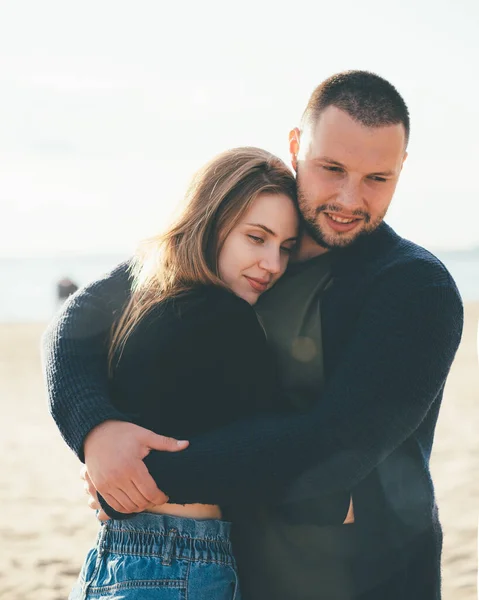 Young adult couple standing on coast and huging each other. Handsome smiling man embracing woman