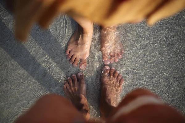 The feet of two people who soak in the beach