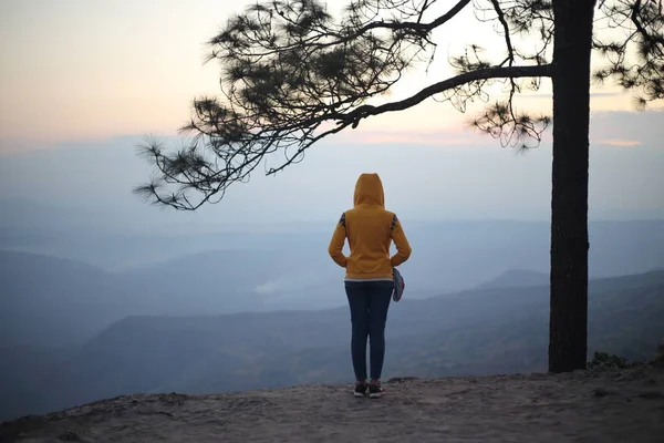 Woman standing on a cliff waiting for sunrise in Phu Kradueng National Park, Loei, Thailand