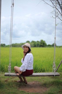 Rayong, Tayland 'da pirinç tarlasında salıncakta oturan bir kadın.
