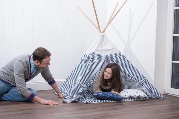 Father and daughter playing at home with constructed wigwam