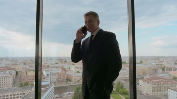 Зрелый Бизнесмен Разговаривает Мобильному Телефону Улыбается Стоя Окна Офиса Видом — стоковое видео