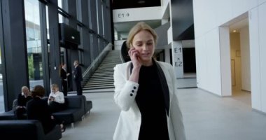 Cam ofis binası salonunda yürüyüş telefonda konuşurken iş kadını