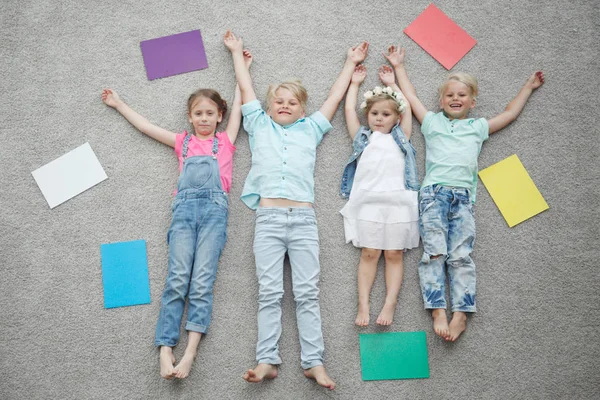 Cuatro Niños Felices Tirados Suelo Sonriendo Entre Papel Colorido —  Fotos de Stock