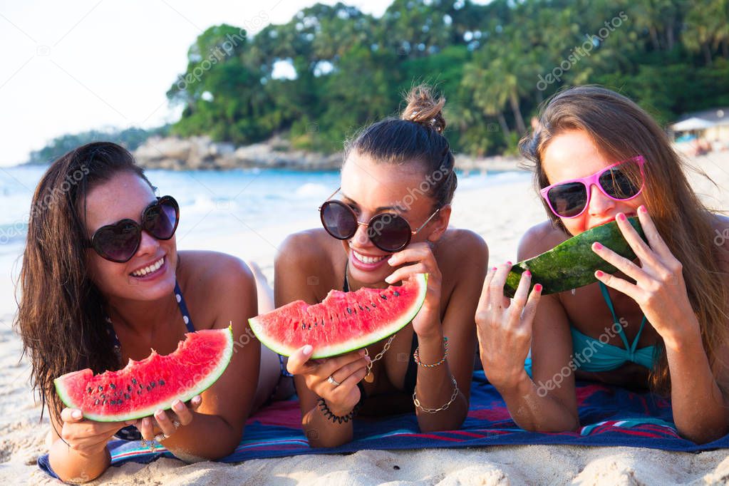Happy smiling female friends eating watermelon on beach