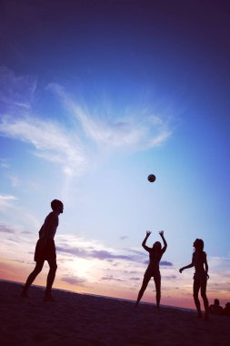 Gün batımında plajda voleybol oynayan bir grup genç.