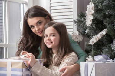 Anne ve kızı yılbaşı ağacının yanında yerde oturmuş hediyelerini açıyor.