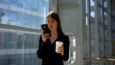 Kahve tutarak ve cep telefonu, net sörf iş merkezinde yürüyüş iş kadını