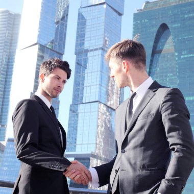 İş adamları gökdelen arka planında el sıkışıyor