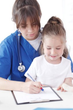 Çocuk hasta ve genç bayan doktor teşhis yazıyorlar.