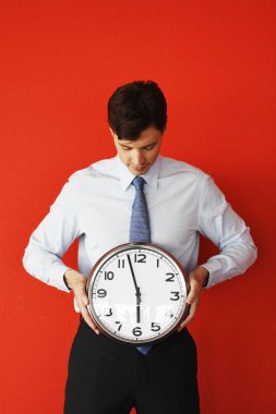 Duvar saati kırmızı zemin üzerine tutarak iş adamı. Zaman, zaman karşı yarış tarafından çalışan zamanımız tükeniyor, iş, çalışan zaman, zaman zaman para kavramı değil gider