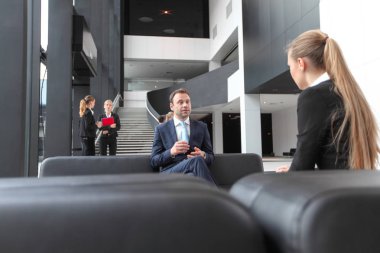 İş adamları ofis lobisindeki koltukta oturup sohbet ediyorlar. Mola, röportaj kavramı.