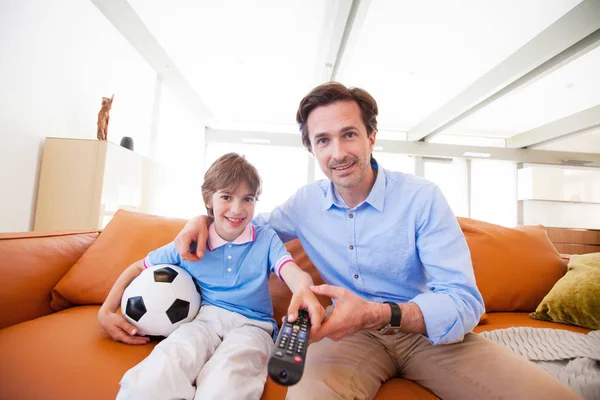 与父亲坐在沙发上看足球比赛的快乐男孩的画像 — 图库照片