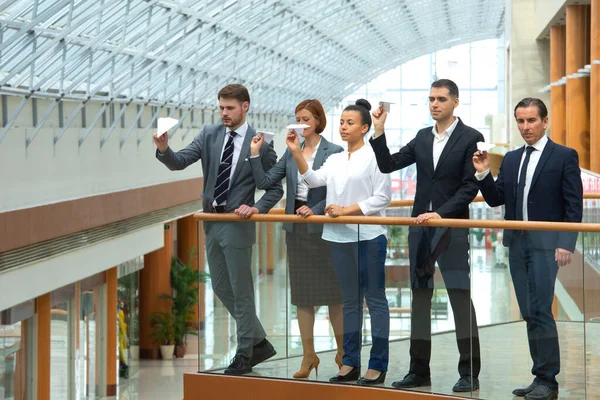 近代的なオフィスビルに紙飛行機を一緒に投げるビジネスの人々のチーム — ストック写真