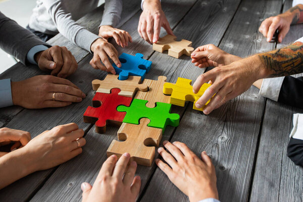 Business people team sitting around meeting table and assembling color jigsaw puzzle pieces unity cooperation ideas concept