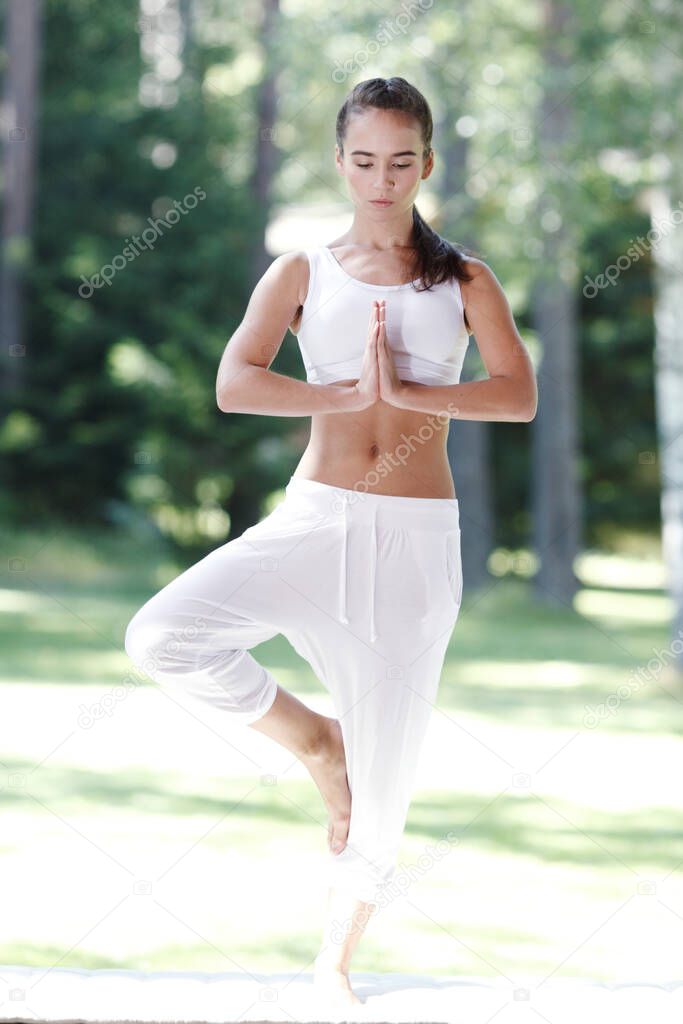 Young woman in white sportswear doing yoga exercise outdoors