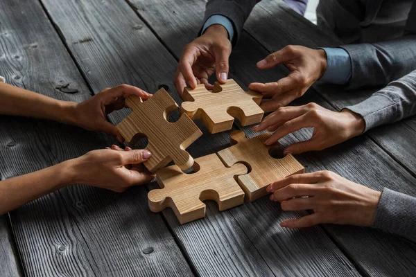 İş adamları masasında oturup ahşap yapboz parçaları birleştirerek işbirliği fikirleri kavramını oluşturuyorlar.