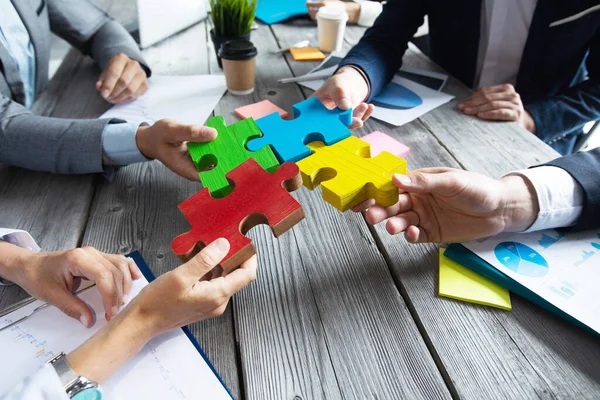 Business people team sitting around meeting table and assembling color jigsaw puzzle pieces unity cooperation ideas concept