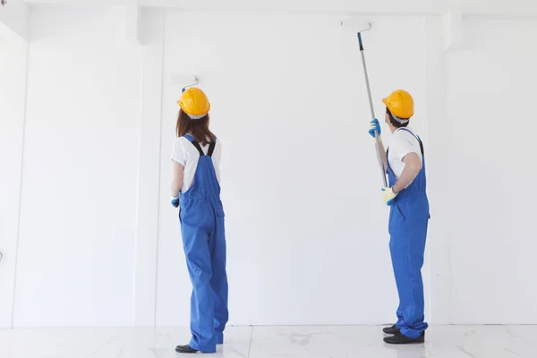 Dois Jovens Trabalhadores Uniforme Macacão Hardhat Pintura Parede Branca — Fotografia de Stock