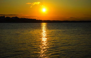 Sahilde günbatımı. Ufukta şehrin ana hatları görebilirsiniz.