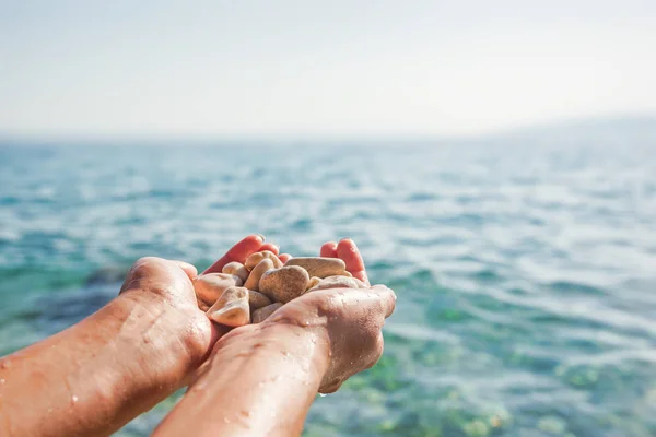 Frauenhände auf dem Hintergrund von Meer oder Ozean halten Meeressteine. — Stockfoto