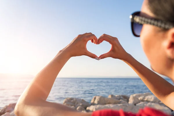 Junge weibliche schöne Hände auf dem Hintergrund des Meeres zeigen das Symbol des Herzens. Urlaub - Konzept. — Stockfoto