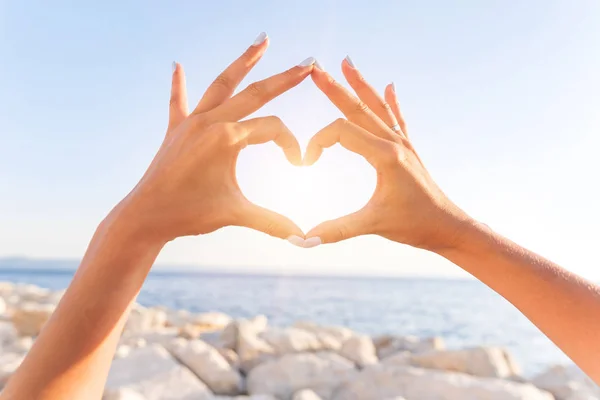 Junge weibliche schöne Hände auf dem Hintergrund des Meeres zeigen das Symbol des Herzens. Urlaub - Konzept. — Stockfoto