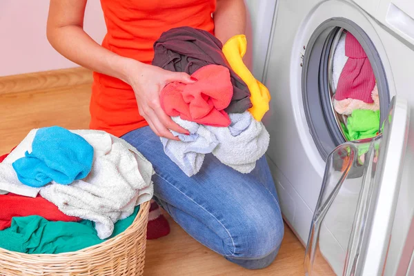 Junge Frau lädt die Wäsche vor dem Waschen aus dem Wäschekorb in die Waschmaschine. — Stockfoto
