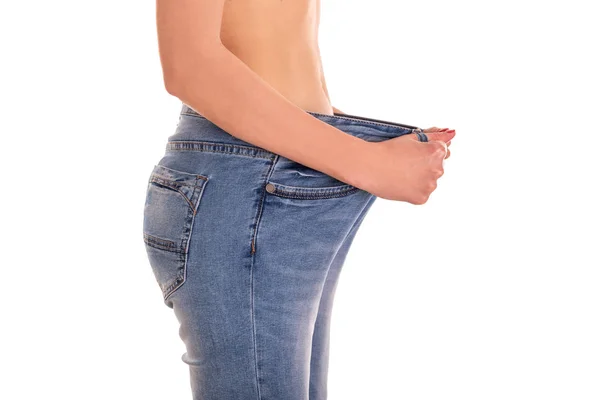 Молода жінка показує струнку фігуру, що витягує великі джинси на білому тлі . — стокове фото