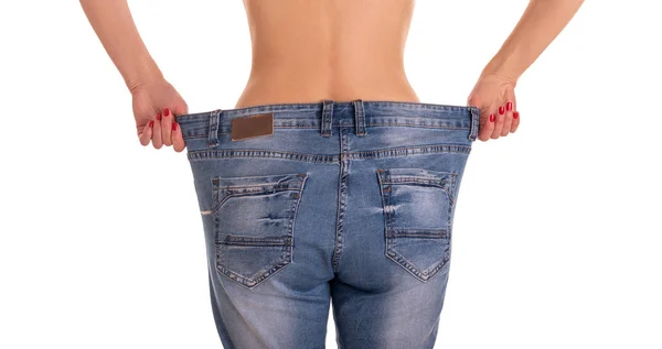 Jeune femme montre une silhouette mince tire de gros jeans sur un fond blanc . — Photo