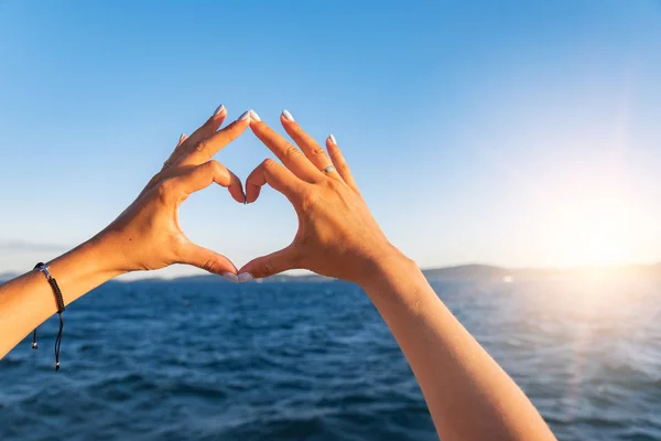 Junge weibliche schöne Hände auf dem Hintergrund des Meeres zeigen das Symbol des Herzens. Urlaub - Konzept. — Stockfoto