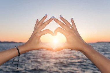 Genç kadın güzel elleri deniz arka plan üzerinde kalp simgesi göster. Tatil - kavram.