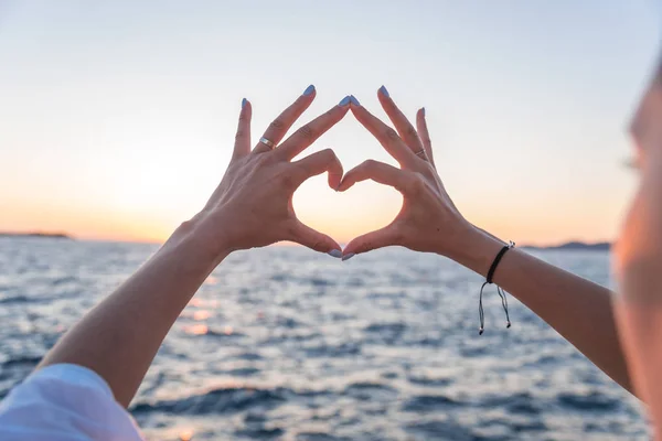 海の背景に若い女性の美しい手は、心のシンボルを表示します。休暇 - コンセプト. — ストック写真