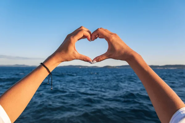 Junge weibliche schöne Hände auf dem Hintergrund des Meeres zeigen das Symbol des Herzens. Urlaub - Konzept. — Stockfoto