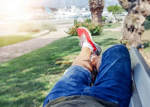 A man in summer clothes and sneakers is lying on a bench in the warm season. — Stock Photo, Image