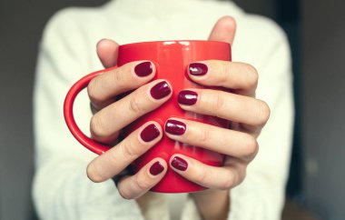 Genç bir kadın elinde sıcak bir içecekle bir bardak tutuyor..