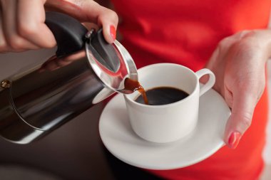 Bir kadın kahve makinesinden bir bardağa kahve döker..