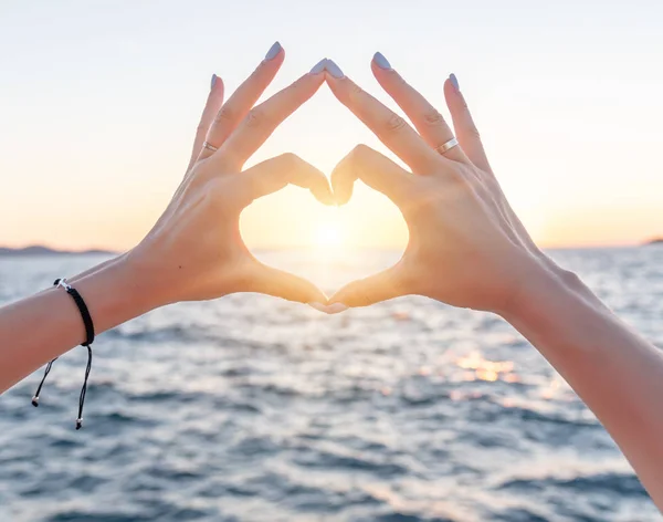 海の背景に若い女性の美しい手は、心のシンボルを表示します。休暇 - コンセプト. — ストック写真