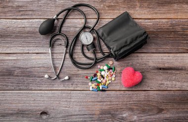 Ahşap arka plan üzerinde tonometre hapları ve kalp modeli.
