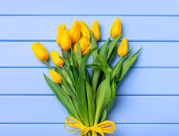 A bouquet of yellow tulips on a table of blue wooden boards.