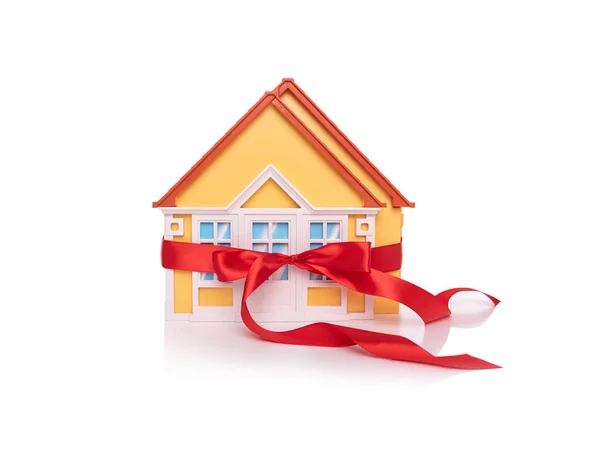 Modelo de casa de juguete vendado con una cinta roja sobre fondo blanco . — Foto de Stock