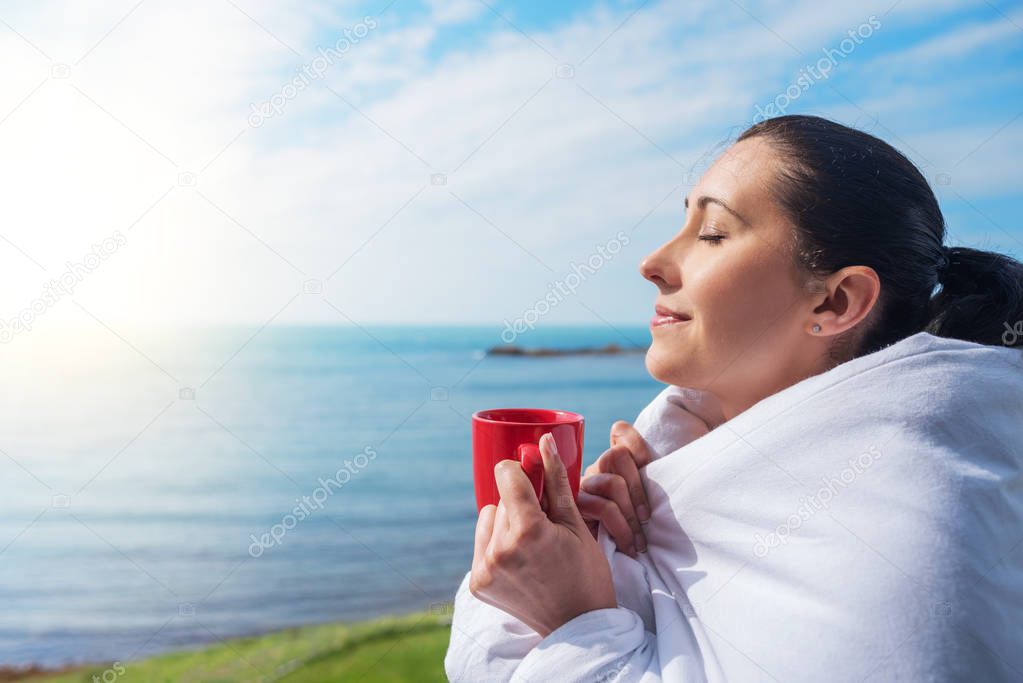 Girl wrapped in a blanket on the balcony in the morning drinks coffee or tea.