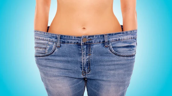 Slender girl in big jeans on a blue background. Losing weight. — Stock Photo, Image