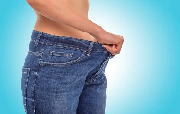 Струнка дівчина у великих джинсах на синьому фоні. Втрата ваги . — стокове фото