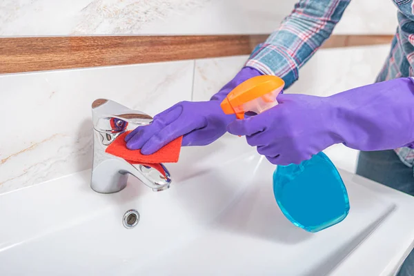 Reinigung im Badezimmer. Eine Frau wischt Waschbecken und Wasserhahn ab. — Stockfoto